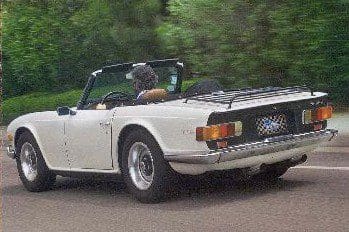 Classic white convertible car driving on a tree-lined road.
