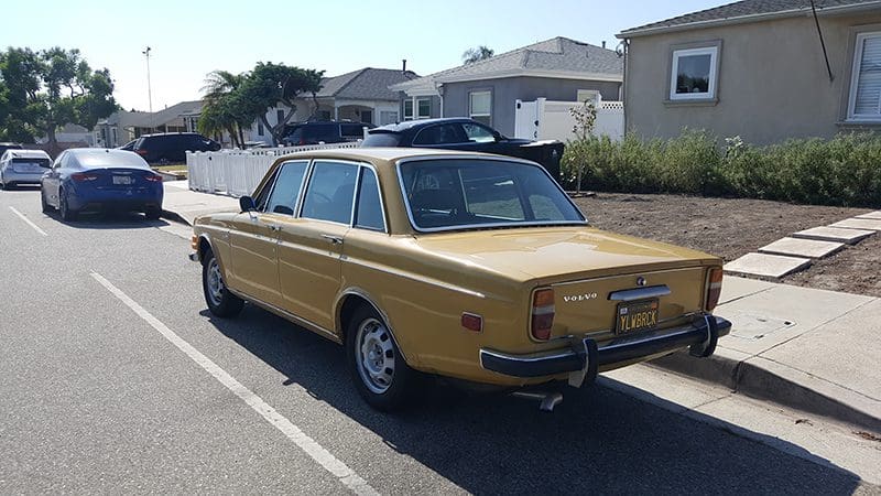 Vintage yellow Volvo 164 parked in a sunny suburban neighborhood.