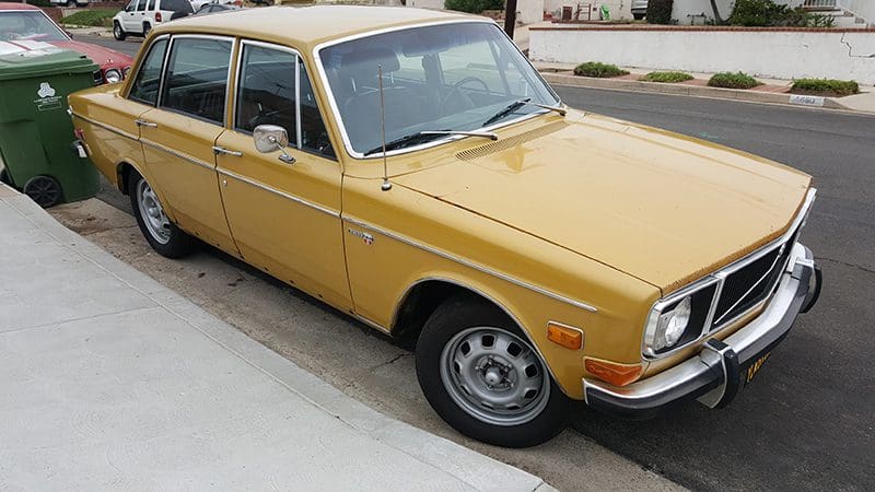 A vintage yellow Volvo sedan parked on a driveway.