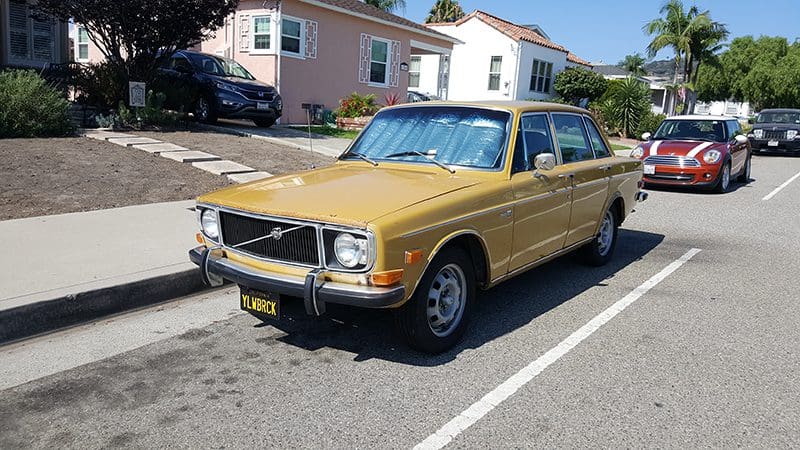 A vintage gold Volvo parked on a residential street in front of houses.