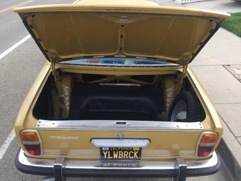 Open trunk of a yellow vintage car showing its interior.