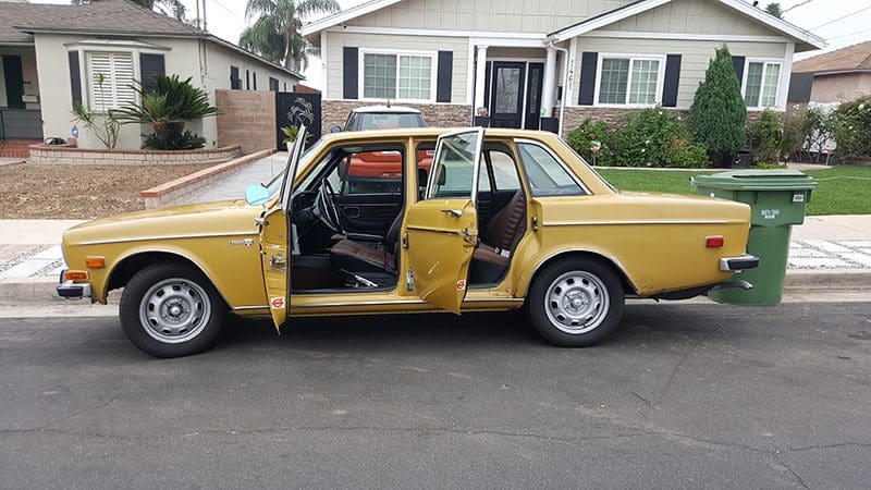 A yellow vintage car with both front and back doors open on the driver's side.