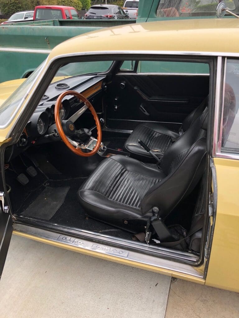 Classic car interior with wooden steering wheel and black leather seats.