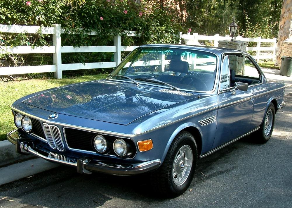 Classic blue BMW convertible parked near a white fence.