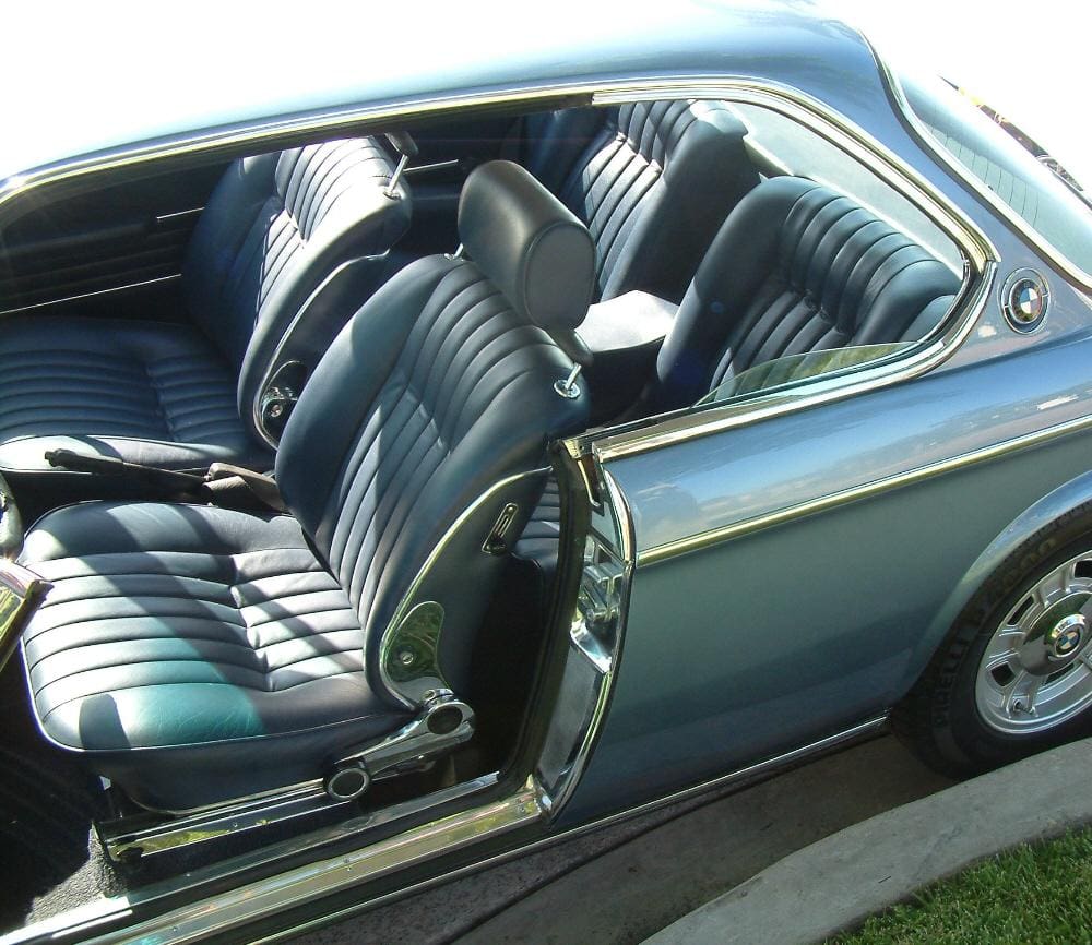Open door shows black leather seats in a vintage car.