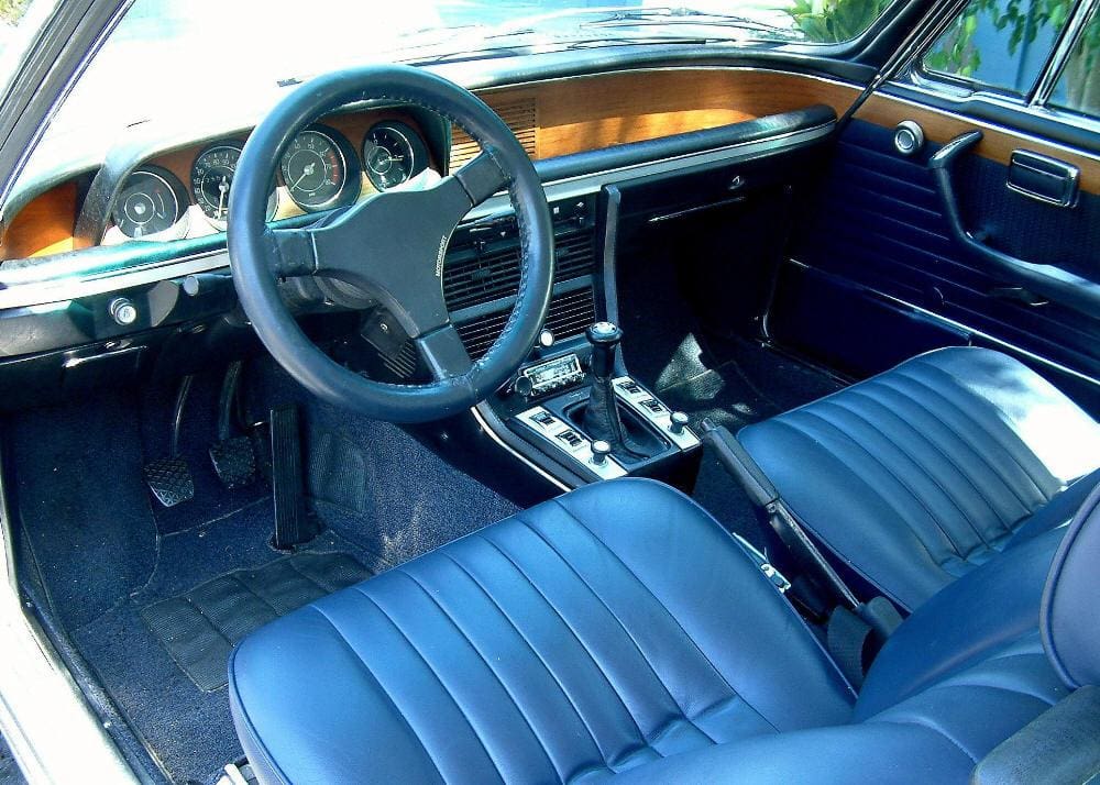 Classic car interior with blue leather seats and wooden dashboard.
