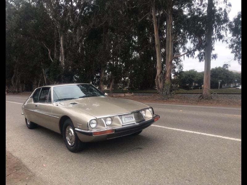 Classic silver car parked by a tree-lined road.