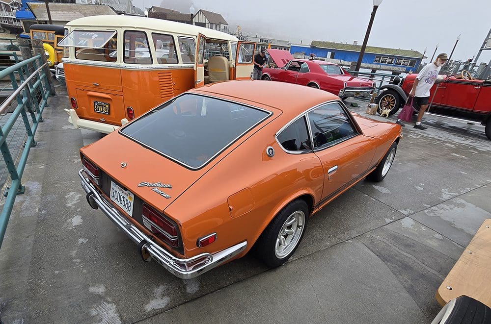 Orange classic sports car parked outdoors on a rainy day.