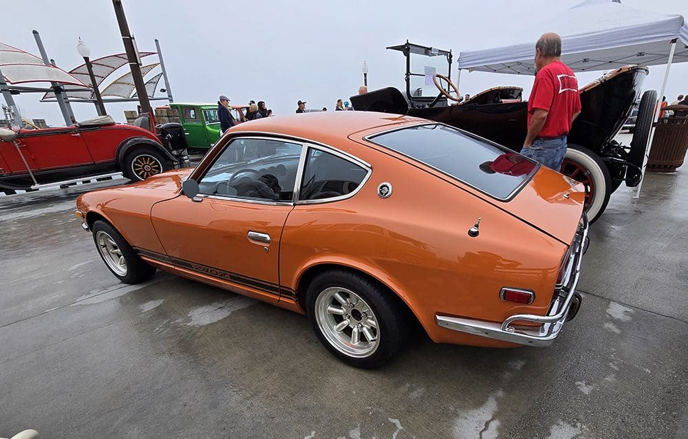 Orange vintage sports car parked outdoors with a person nearby.