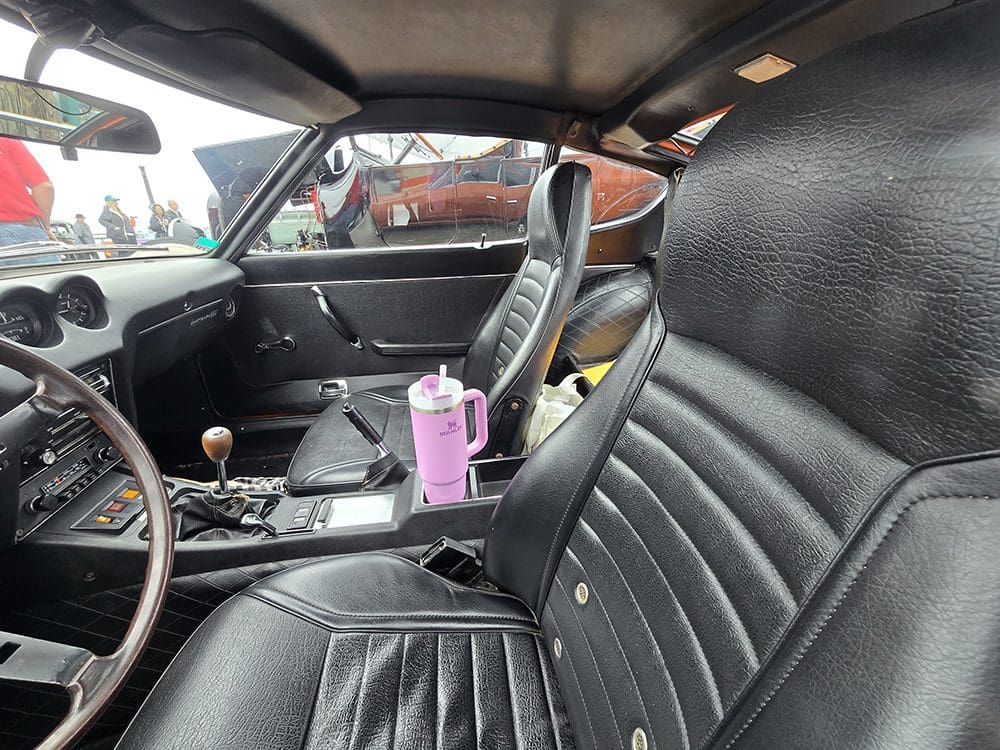 Interior of a classic car with black leather seats and a pink air freshener.