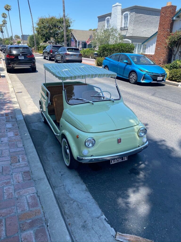 A vintage green microcar parked on a sunlit street.