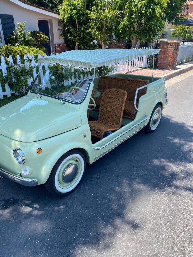 A vintage small car with an open side door is parked outdoors.