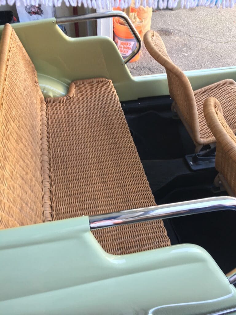Close-up of a vintage car seat with woven upholstery and metal armrest.