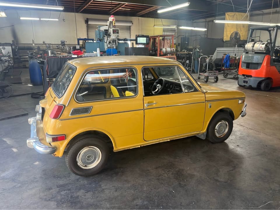Vintage yellow compact car parked indoors in a workshop.