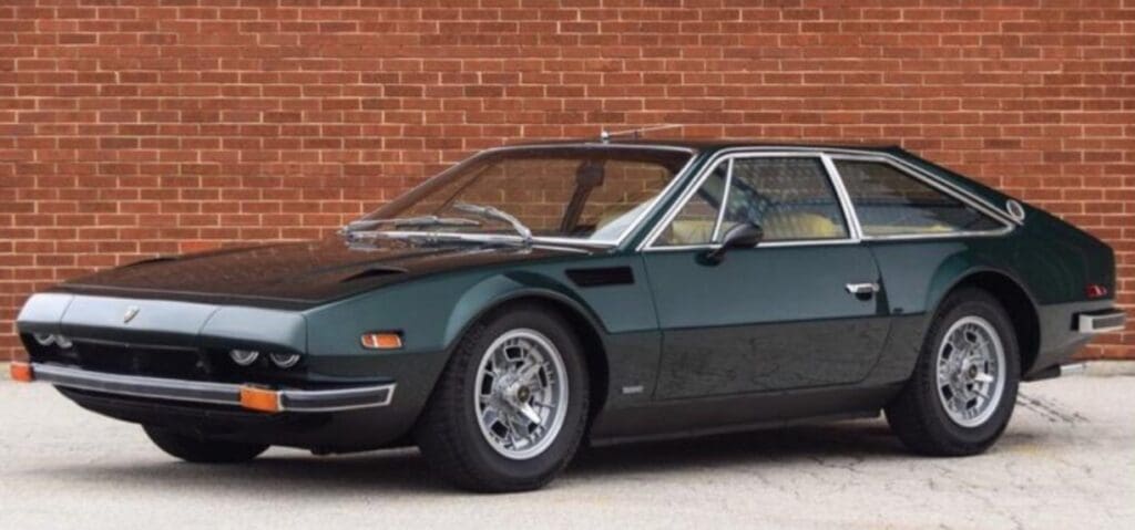 Classic green sports car parked beside a red brick wall.