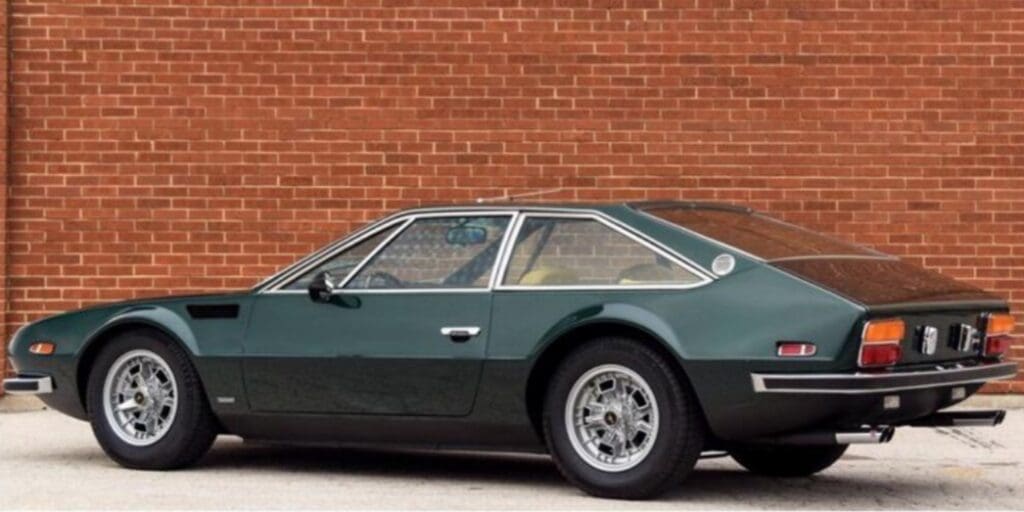 Classic dark green sports car parked by a brick wall.