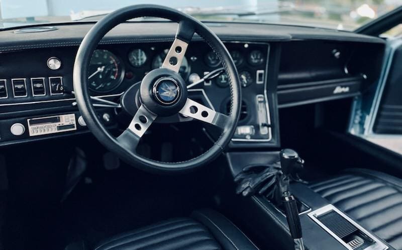 Classic car interior with a vintage steering wheel and dashboard.