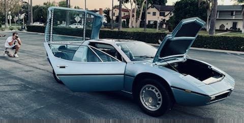 Classic silver sports car with doors and hood open in a parking lot.