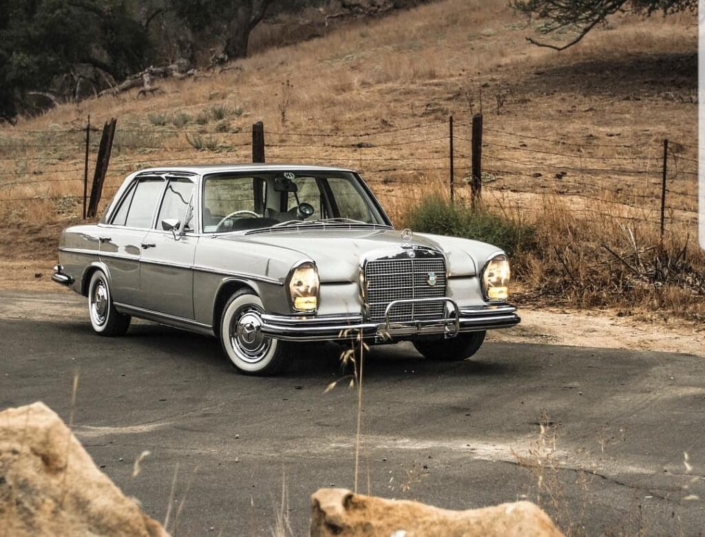 Classic silver Mercedes-Benz parked by a rural fence on a dirt hill.