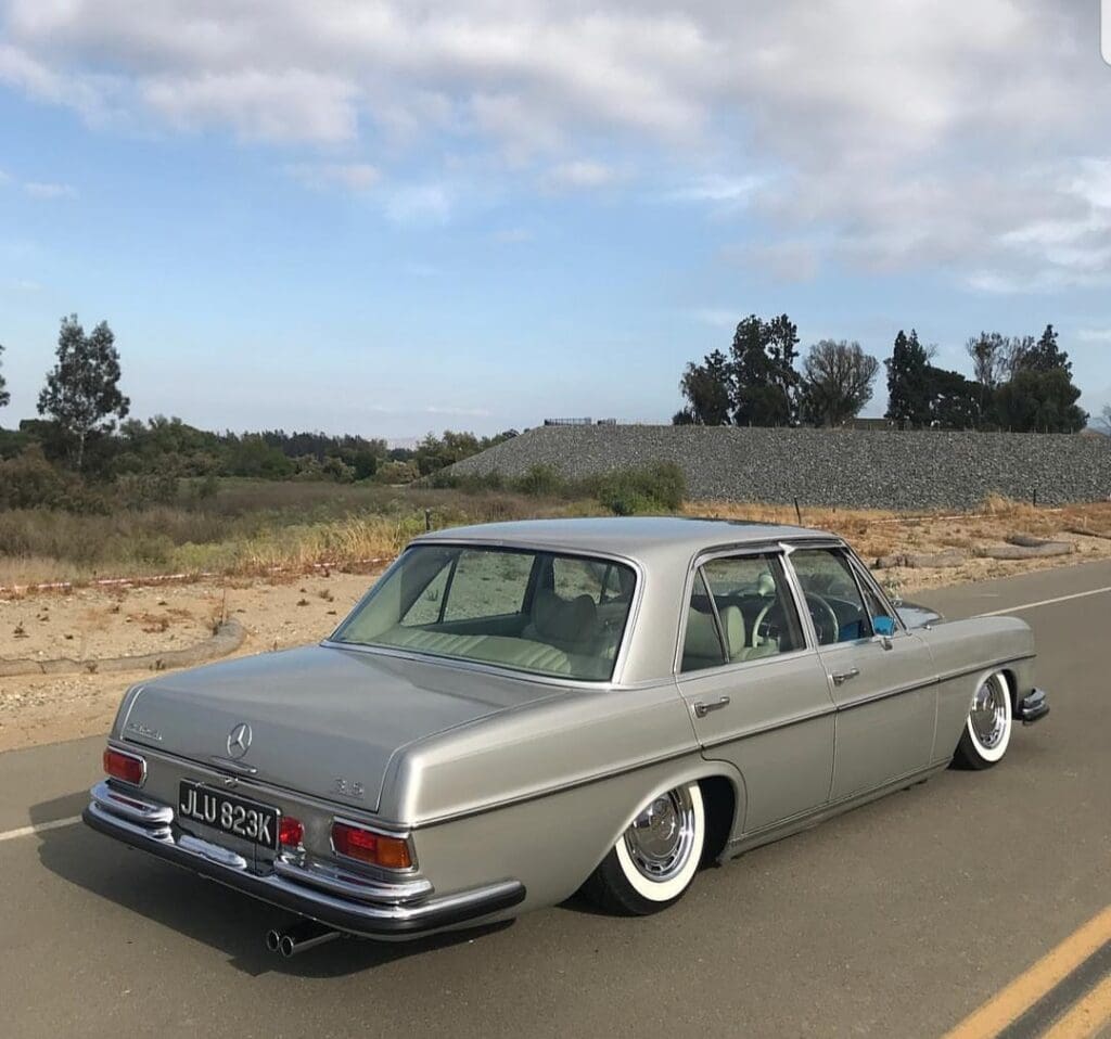Classic silver vintage car parked on a road near a sandy area.