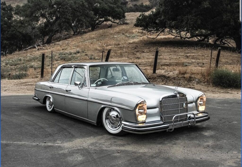 Classic silver Mercedes-Benz parked on a rural road beside a barbed-wire fence.