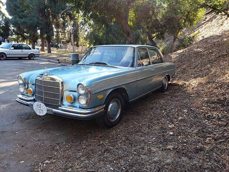 Classic vintage blue Mercedes-Benz parked in a wooded area.