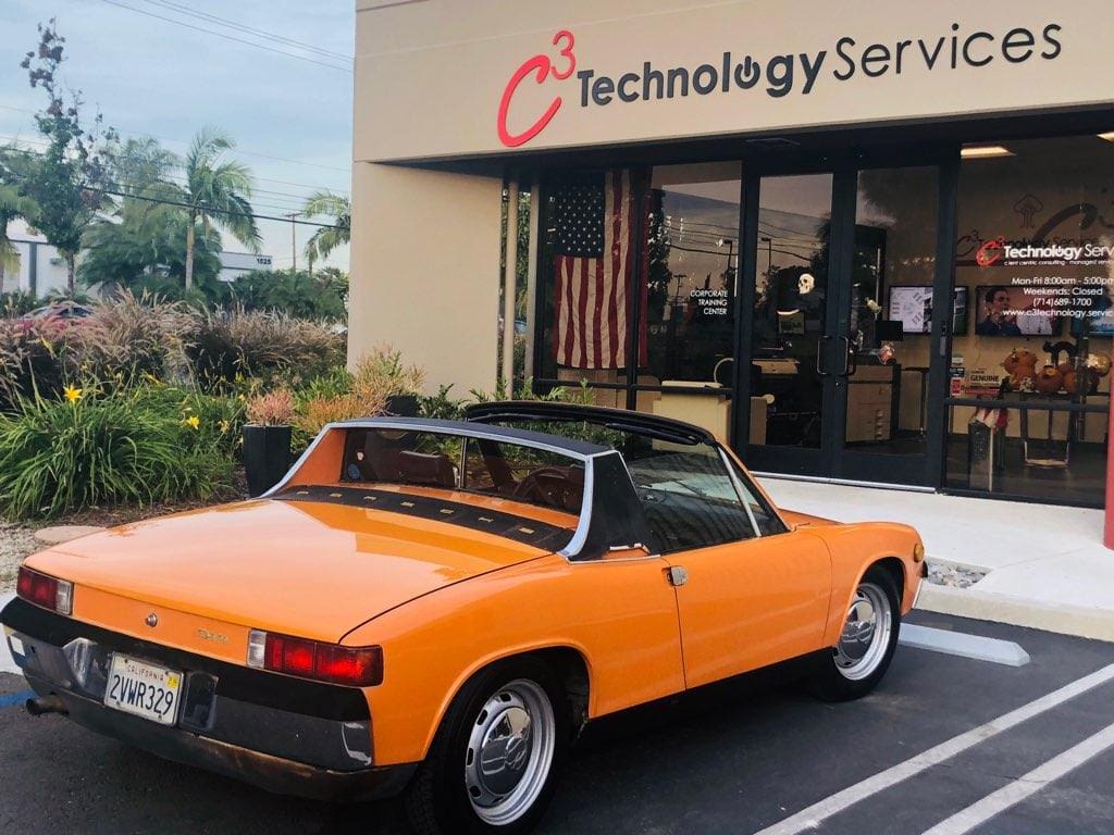 Orange classic convertible car parked outside a tech service building.