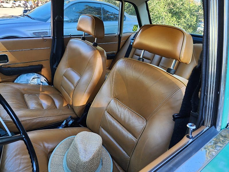 Brown leather seats inside a vintage car with a straw hat resting on the passenger seat.