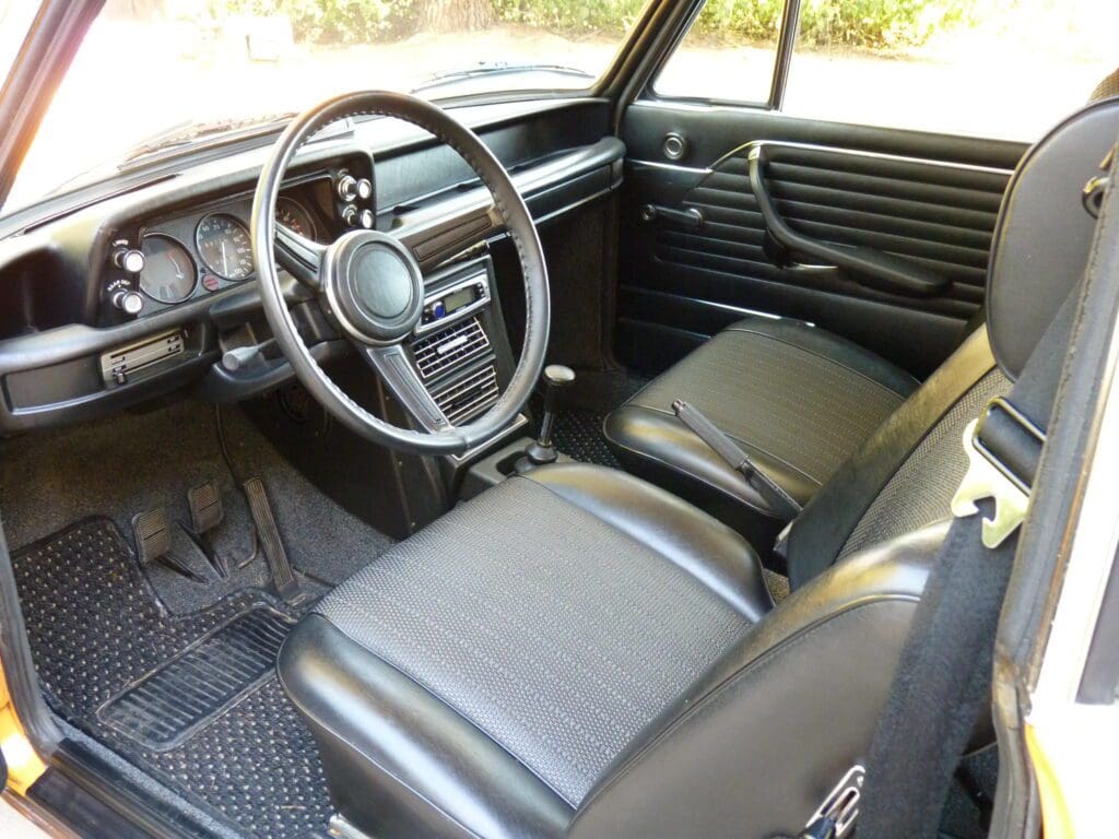 Interior of a classic car with black leather seats and a wooden steering wheel.