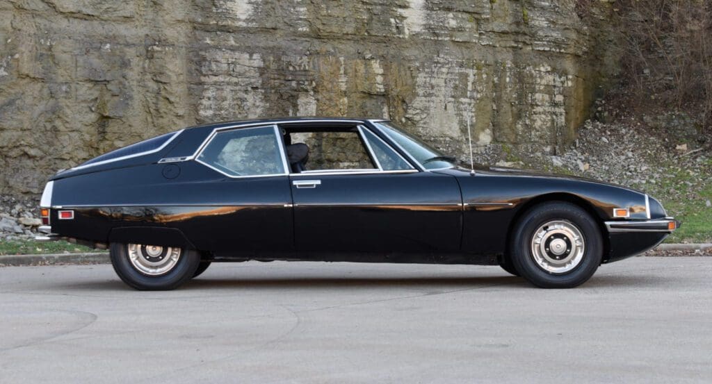 A sleek black classic car parked by a stone wall.