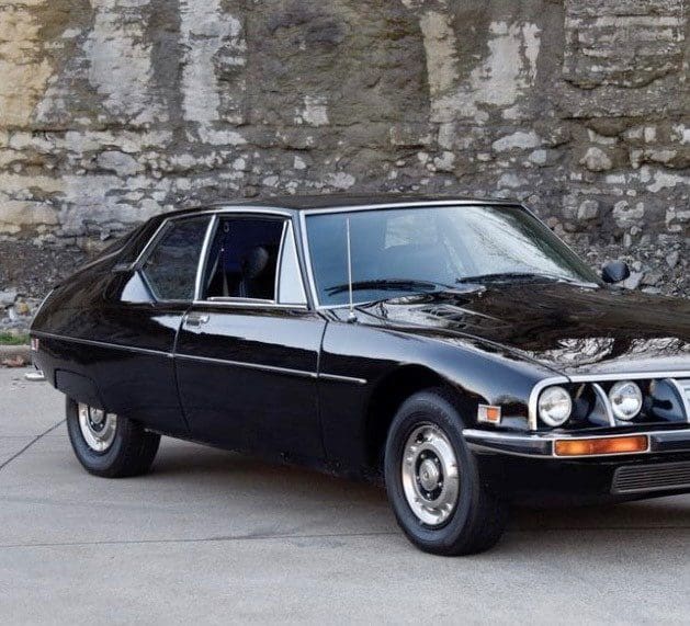 Classic black vintage car parked near a stone wall.