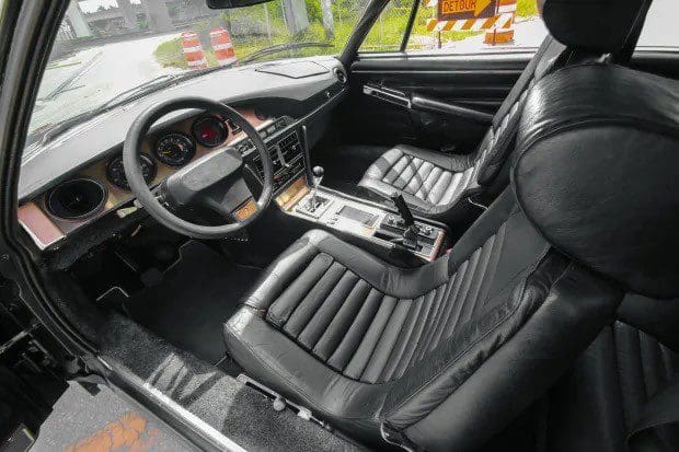 Interior of a classic car with black leather seats and vintage steering wheel.