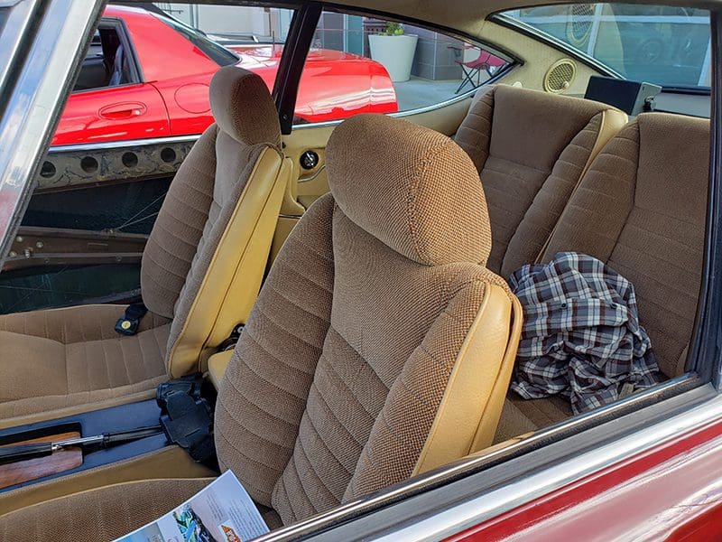 Interior view of a car with beige seats and a red car visible outside.