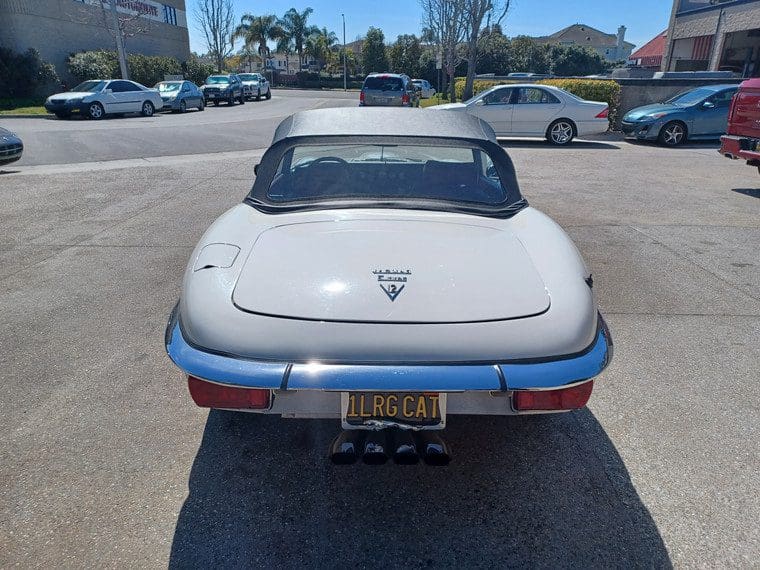 Rear view of a classic white sports car with a soft top in a parking lot.