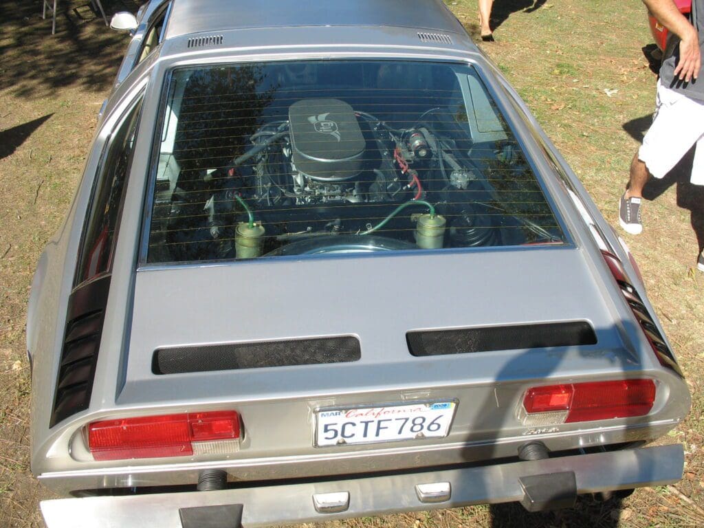 Rear view of a silver sports car with a visible engine through the back window.