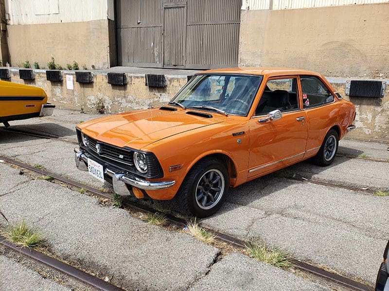 Orange classic car parked on a street near a building.
