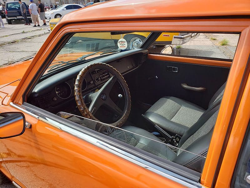 Interior view of a vintage orange car with a classic steering wheel and simple dashboard.