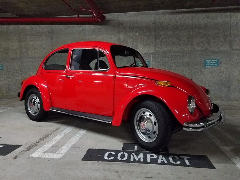 Classic red Volkswagen Beetle parked in a compact spot.