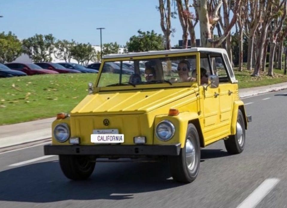 Yellow vintage SUV driving on a road with palm trees.