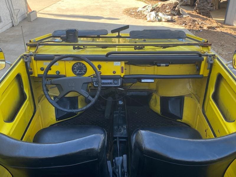 Interior of a vintage yellow vehicle with black seats and a simple dashboard.