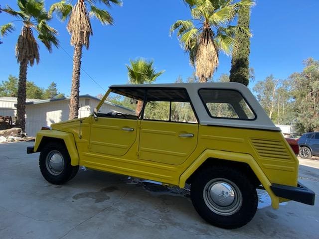 Yellow vintage convertible car parked under palm trees on a sunny day.