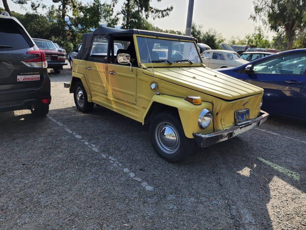 A vintage yellow convertible car parked in a lot with a black soft top.