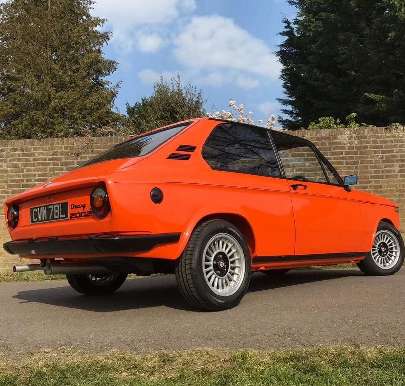 Classic orange sports car parked outdoors on a sunny day.