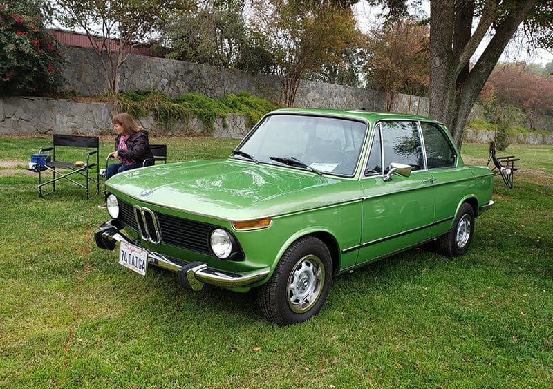 Vintage green BMW parked on grass with a person nearby.