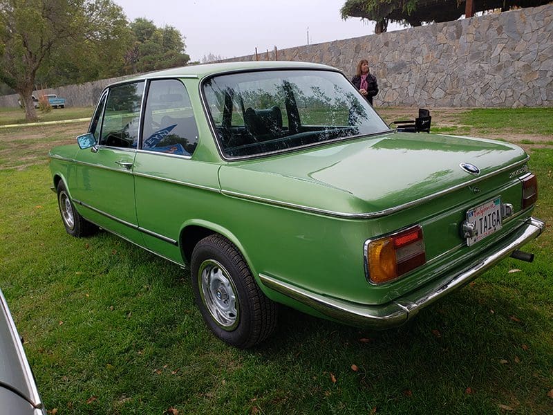 Classic green vintage car parked on grass beside a stone wall.