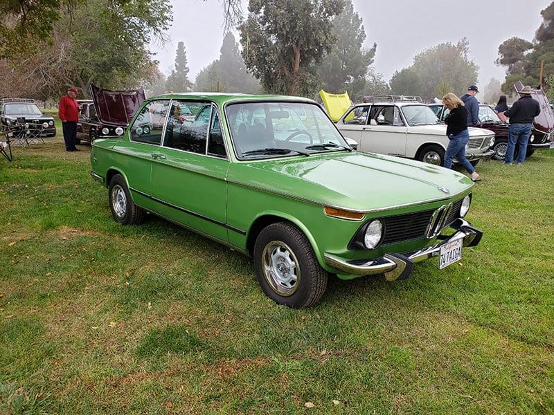 Classic green vintage car parked on grass at an outdoor event.