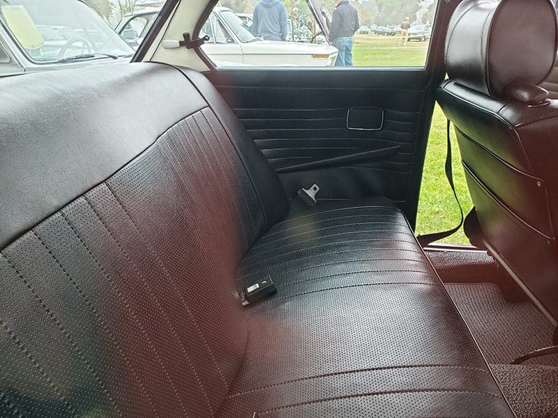 Interior view of a vintage car's backseat with maroon leather upholstery.