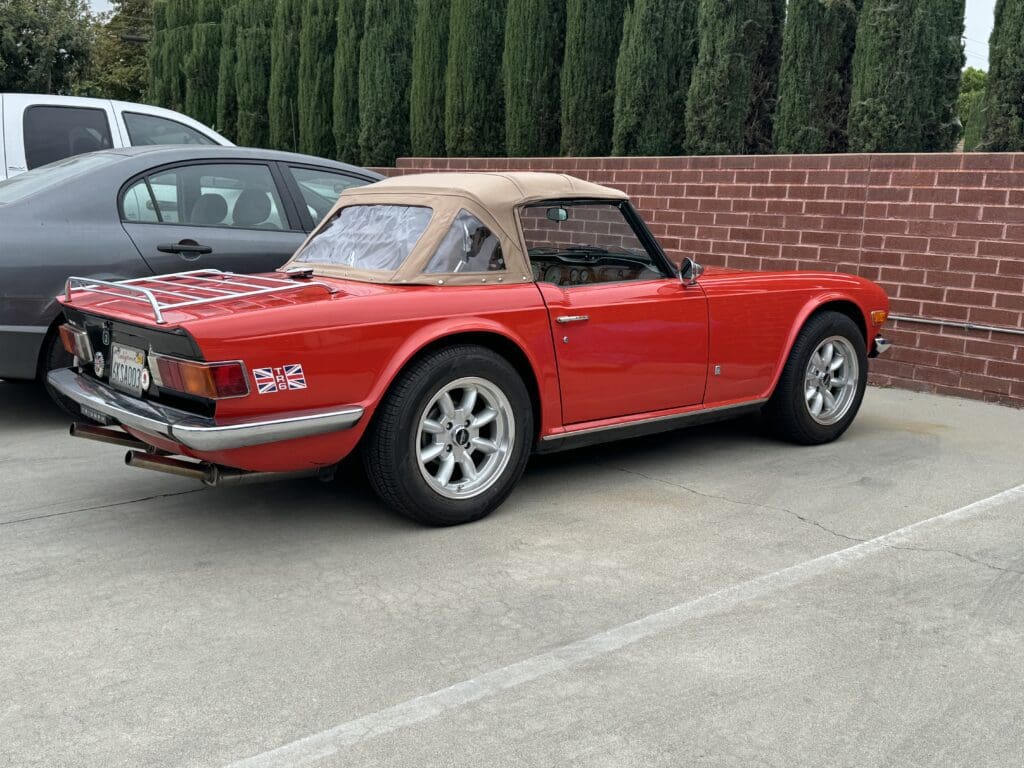 Classic red convertible sports car parked in a lot with a tan soft top.