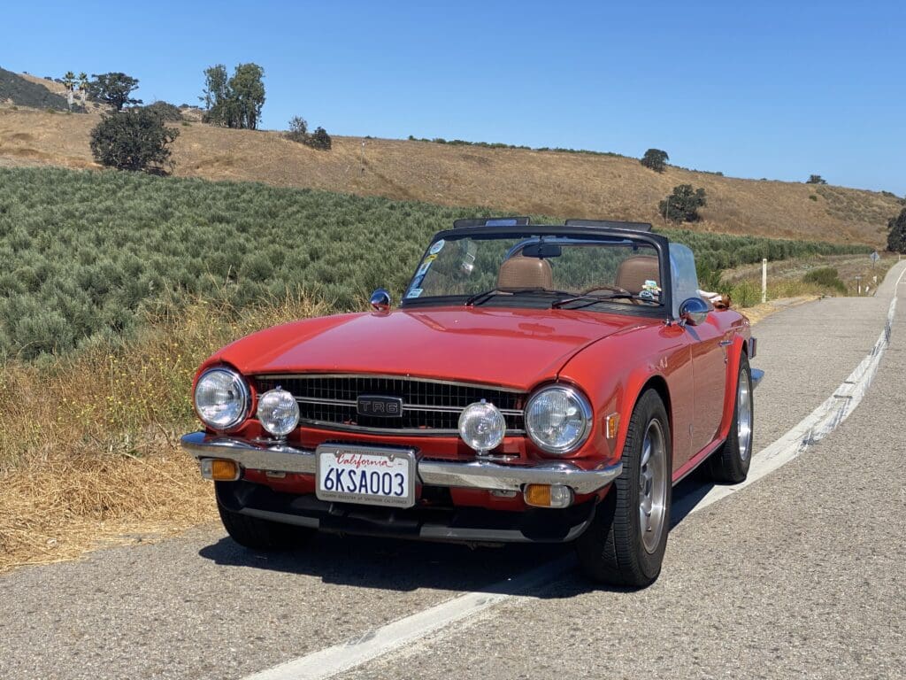 Classic red convertible car parked on a country road under clear blue sky.