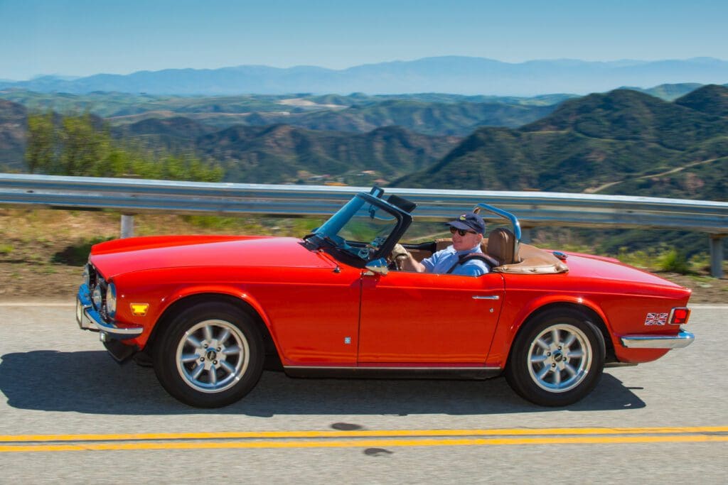 Man driving a red convertible on a mountain road.